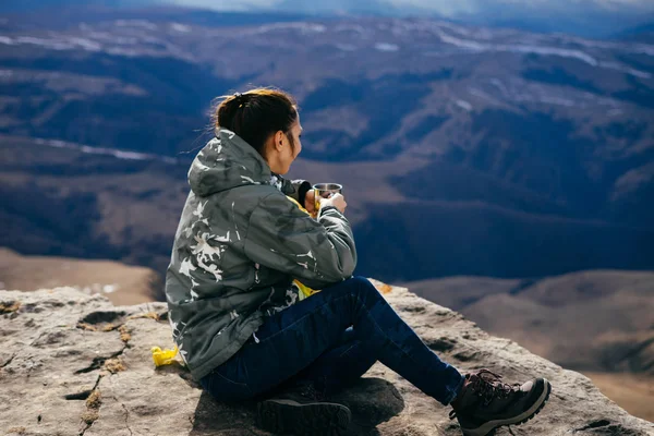 Una joven lleva un estilo de vida saludable y activo, se sienta en el borde del acantilado y disfruta de la naturaleza —  Fotos de Stock