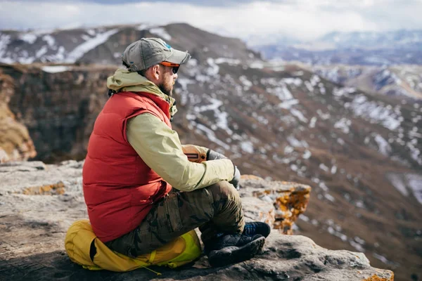 Взрослый мужчина путешествует, сидит на краю скалы и наслаждается природой — стоковое фото