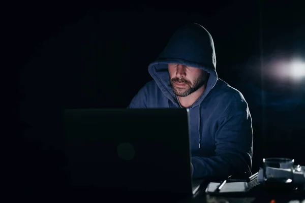 Un uomo adulto criminale nasconde la faccia sotto il cofano, hackera il portatile — Foto Stock