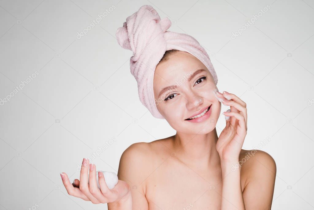 smiling young girl with towel on head applying cleansing foam on face