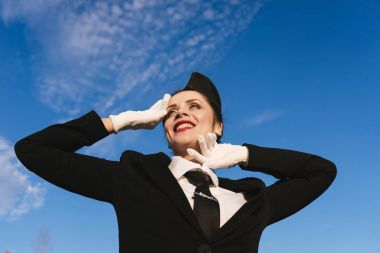 üniformalı mavi gökyüzü altında mutlu gülümseyen kadın hostes uçak için bekliyor