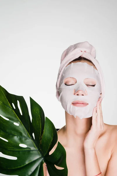 Young girl with a towel on her head, on her face a tissue mask, a spa procedure — Stock Photo, Image