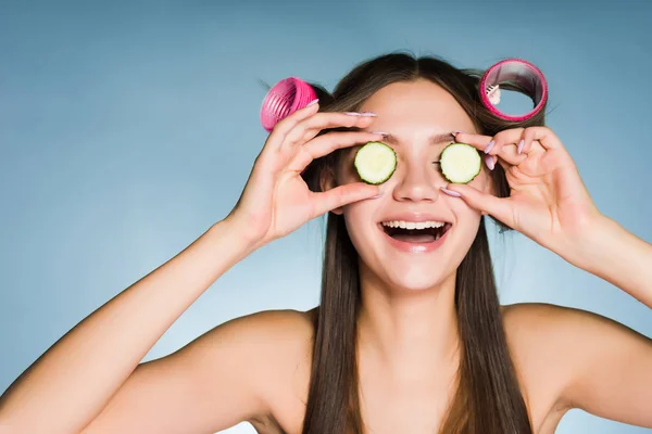 Směje se mladá dívka hospodářství kousky okurky v okolí očí, na hlavě natáčky — Stock fotografie