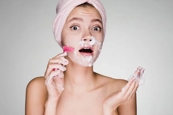 Забавная молодая девушка с розовым полотенцем на голове бреет лицо, как мужчина — стоковое фото