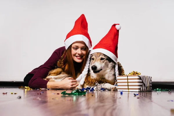 Happy red-haired girl sits on the floor with her dog, christmas atmosphere, tinsel and gifts — Stock Photo, Image