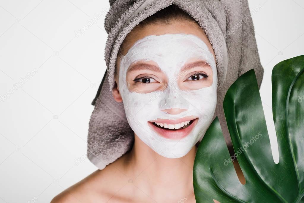 happy smiling girl with towel n agolove applied white nourishing mask on face, spa procedure