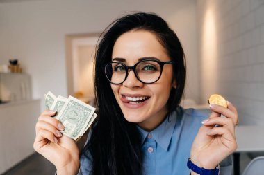 dolar ve altın bitcoin elinde tutan gözlük ve mavi gömlek gülümseyen kız mutlu