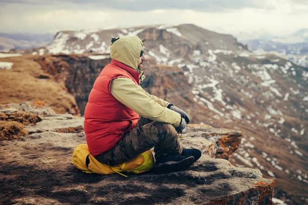 Чоловік-мандрівник сидить на краю гори, відпочиває і насолоджується чистим гірським повітрям — стокове фото