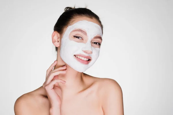 Ένα αστείο κορίτσι χαμογελαστό έχει βάλει στο πρόσωπο μια λευκή θρεπτική μάσκα κατά των ρυτίδων — Φωτογραφία Αρχείου