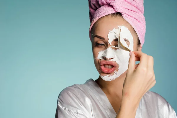 Una joven con una toalla rosa en la cabeza se quita la máscara blanca de la cara —  Fotos de Stock