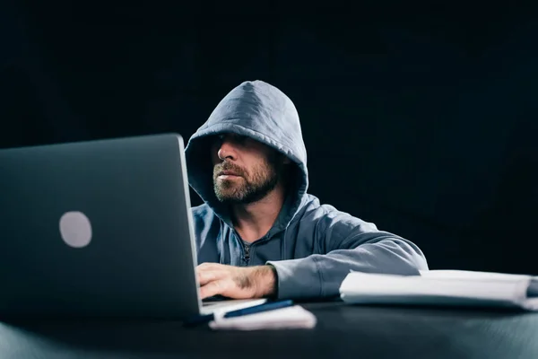 Orang berjenggot kriminal menyembunyikan wajahnya di bawah kap mesin, melakukan sesuatu yang ilegal pada laptop ... — Stok Foto