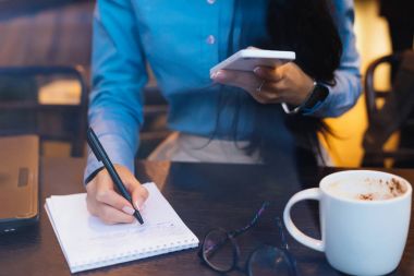 genç kız telefonda elele defterini notlar yapar