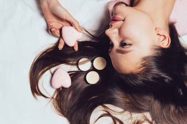 Chica joven se encuentra en la cama mirando guijarros en forma de corazón —  Fotos de Stock