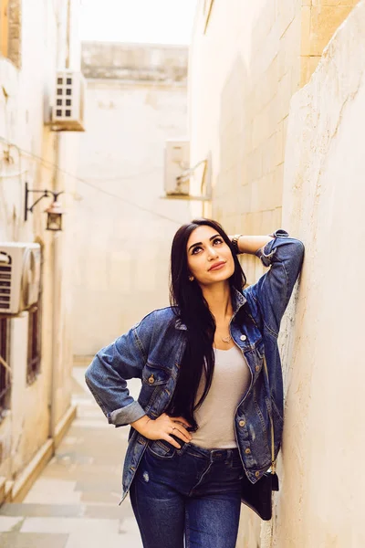 A young girl in a jeans suit walks the old streets of the city — Stock Photo, Image