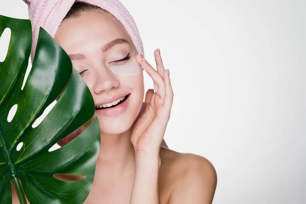 Gelukkig meisje met een handdoek op haar hoofd geldt een hydrogel masker onder de ogen — Stockfoto