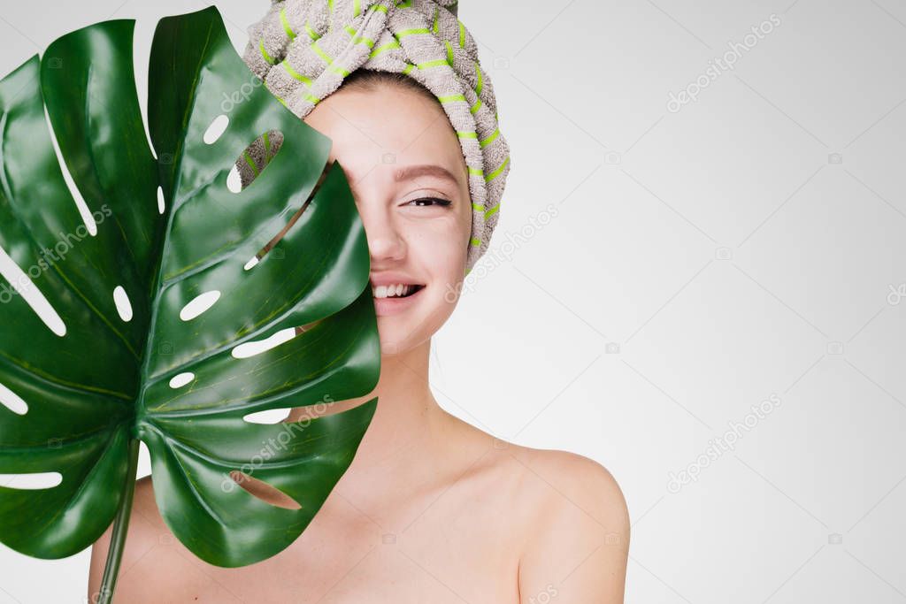 young girl on a white background smiling hiding behind a large leaf of a plant