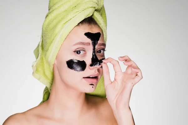 Chica con una toalla en la cabeza quita una máscara facial de limpieza negro — Foto de Stock