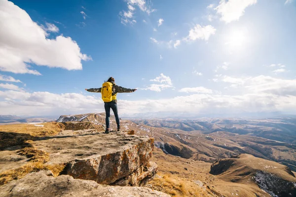 Girl tourist with her big backpack spread her hands against the background of the mountains on a sunny day — Stock Photo, Image