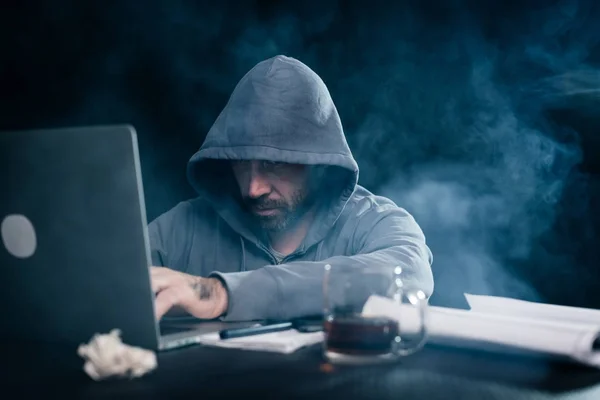 Pria dengan jenggot hacker di kaus dengan kerudung duduk di belakang laptop — Stok Foto