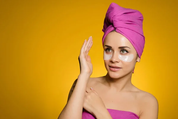 Jovem atraente com uma toalha rosa na cabeça pensando sobre a beleza, sob os olhos de manchas — Fotografia de Stock