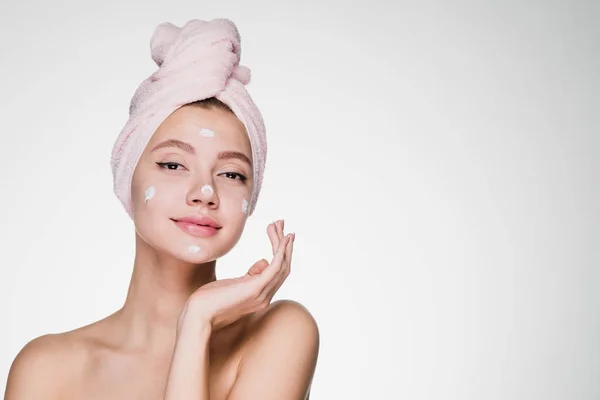 Милая привлекательная девушка с розовым полотенцем на голове, применяя белый увлажнитель на лице — стоковое фото