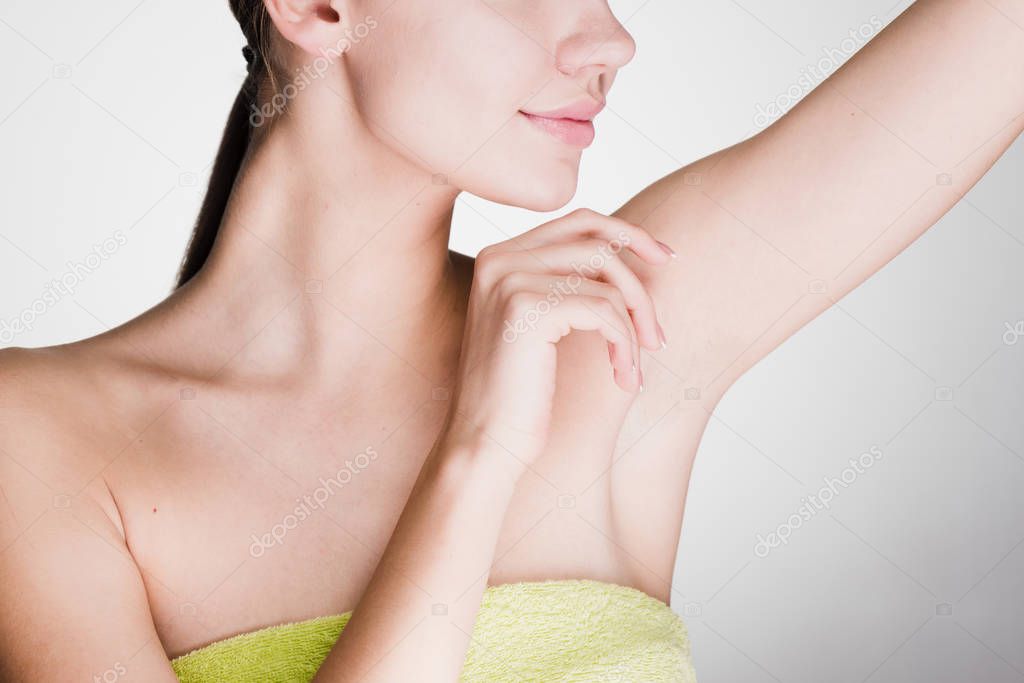 A young girl in a towel after a shower looks after the skin of her armpits