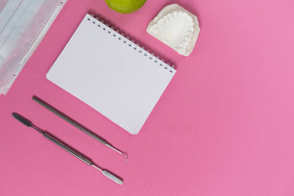 на розовой поверхности находятся стоматологические инструменты, белая подушка и гипсовый слепок зубов
