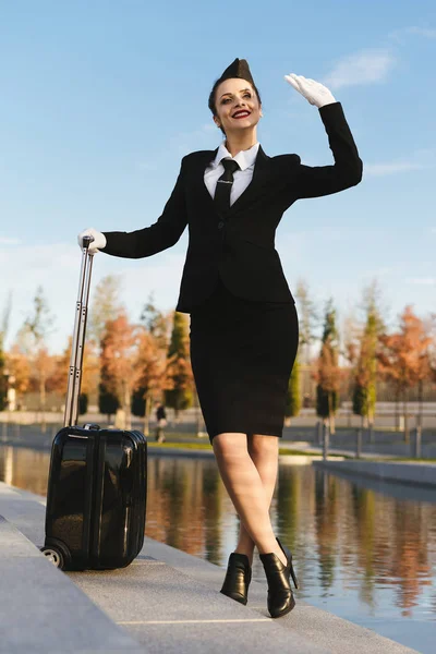 Jistotu, že letuška krásná žena v uniformě vypadá až do nebe, s kufrem — Stock fotografie