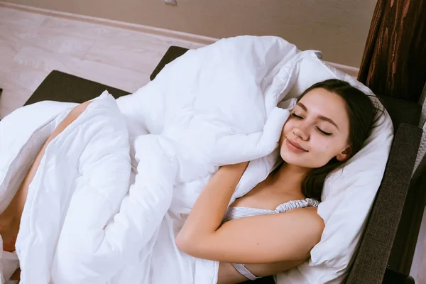 Linda chica joven durmiendo, acostado en la cama bajo una manta blanca — Foto de Stock