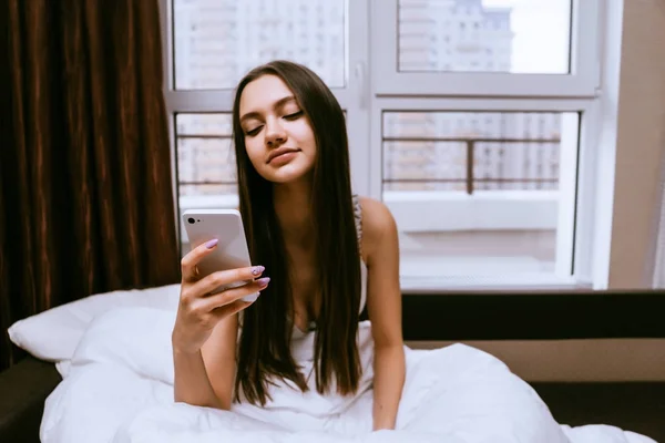 Una joven se despertó por la mañana y sostiene un teléfono — Foto de Stock