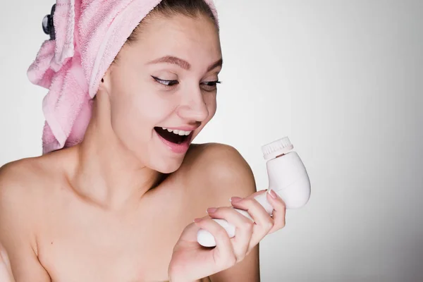 Ung flicka med en handduk på huvudet håller en anordning för rengöring av huden leende — Stockfoto