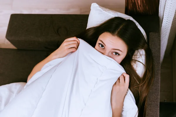 Mladá dívka leží na posteli, schovává pod dekou — Stock fotografie