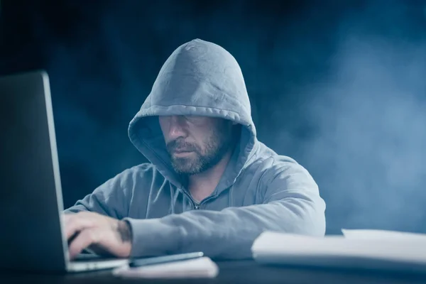 Misterioso barbudo homem esconde seu rosto sob o capô, hacks o laptop — Fotografia de Stock