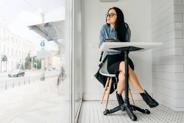 Девушка в очках сидит за столом на фоне большого окна — стоковое фото