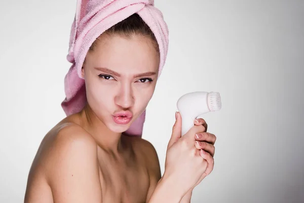 Meisje met een handdoek op haar hoofd een elektrische borstel voor het reinigen van haar gezicht te houden — Stockfoto