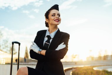 Hostes kız günbatımı arka planda bavulla duruyor