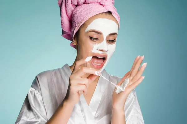 Молодая девушка с полотенцем на голове надевает на лицо белую маску — стоковое фото