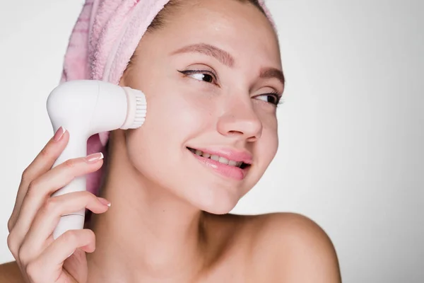 A young girl with a towel on her head cleans the skin with a special device — Stock Photo, Image