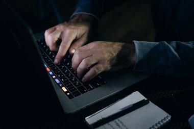 karanlık bir odada oturan bir dizüstü bilgisayar arkasında çalışan deneyimli bir hacker