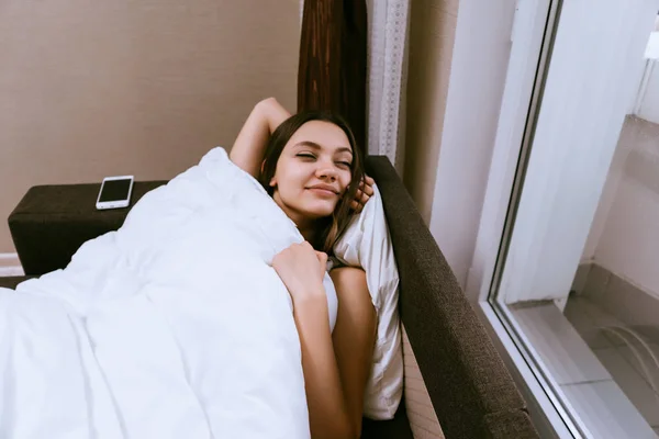 Menina feliz dormindo na cama sob um cobertor — Fotografia de Stock