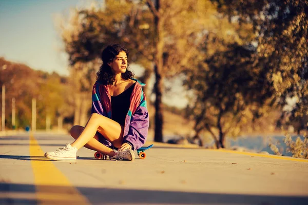 Giovane ragazza si siede su uno skateboard sullo sfondo della pista — Foto Stock