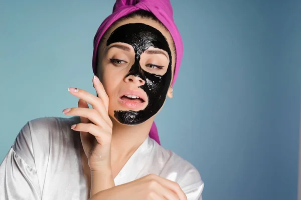 Молодая девушка на синем фоне надевает на лицо черную маску — стоковое фото