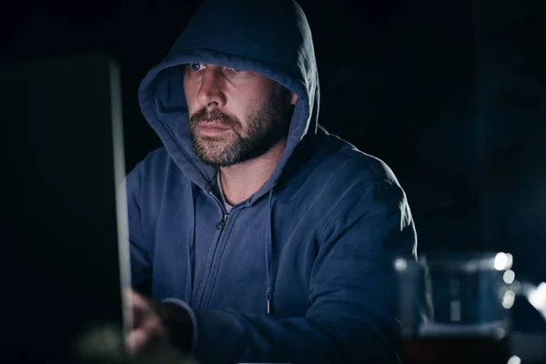 Jovem hacker trabalhando atrás de laptop em casa — Fotografia de Stock