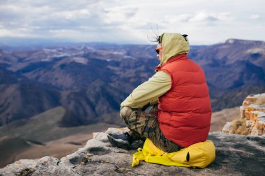 Kapşonlu ceket bir adam oturuyor ve Dağları görünüyor
