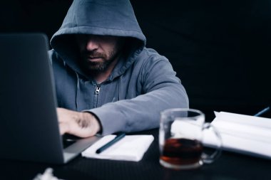 Genç bir hacker düşünceli bir bardak çay ile bir dizüstü bilgisayar arkasında çalışma