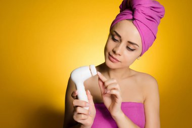 Genç bir kızın kafasındaki bir havlu ile cilt temizliği için bir cihaz hazırlanıyor