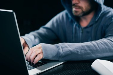 karanlık bir odada bir dizüstü bilgisayar arkasında çalışan bir genç hacker