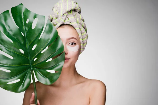 Una joven con una toalla en la cabeza está de pie detrás de una hoja grande de una planta — Foto de Stock