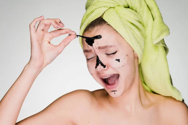 A young girl with a towel on her head with pain relieves a black mask from herself — Stock Photo, Image