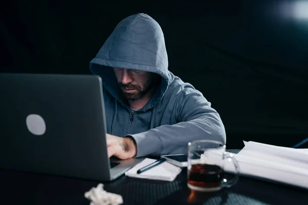 Junge Hacker arbeiten hinter Laptop mit einer Tasse Tee — Stockfoto